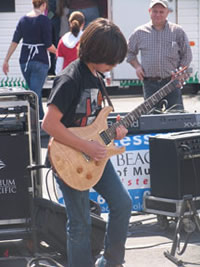 Photo image of Long Beach School of Music guitar student performing at Kids in the Kitchen outdoor fair sponsored by the Junior League of Long Beach